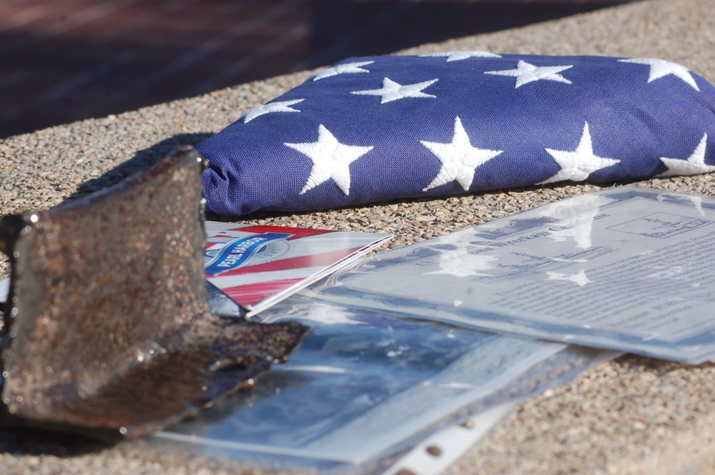 Un pedazo certificado del USS Arizona junto con una bandera americana que voló sobre el Pearl Harbor durante el 65o aniversario del ataque se pone en la exhibición durante la ceremonia de la conmemoración de Pearl Harbor en el cementerio de Tonaquint, St. George, Utah, el 7 de Dic., 2016 | Foto de Hollie Reina, Noticias St. George 